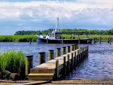 A boat docked by a wooden pier on a calm river under a cloudy sky.