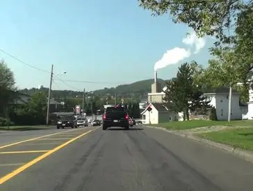 A road with cars driving towards a small town with hills in the background.