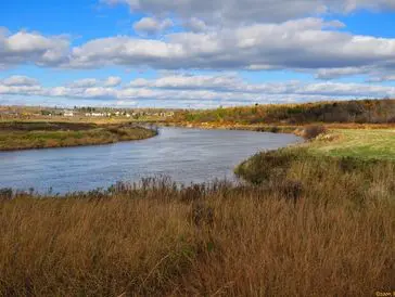 A calm river winding through a grassy landscape under a blue sky.