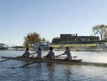 A rowing team of four paddling on a calm river during daytime.