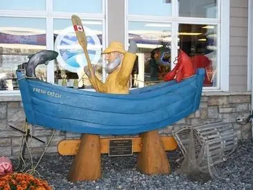 Blue wooden boat sculpture with carved birds and figures outside a building.