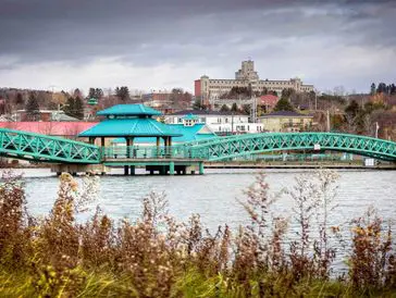 A turquoise pedestrian bridge over a river with a cityscape in the background.