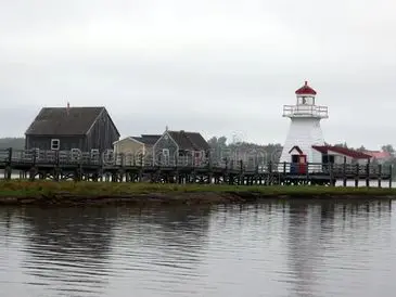 A lighthouse by the water with houses and a cloudy sky.
