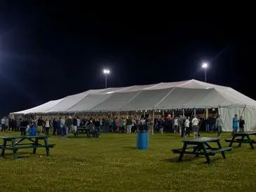 Large crowd gathered under a white tent on a lawn at night.