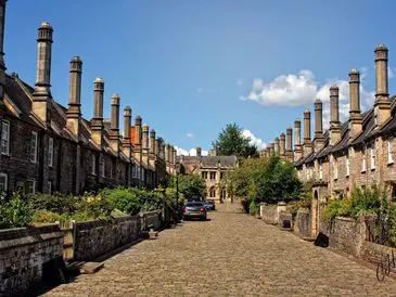 Historic cobblestone street lined with vintage chimneys and greenery.