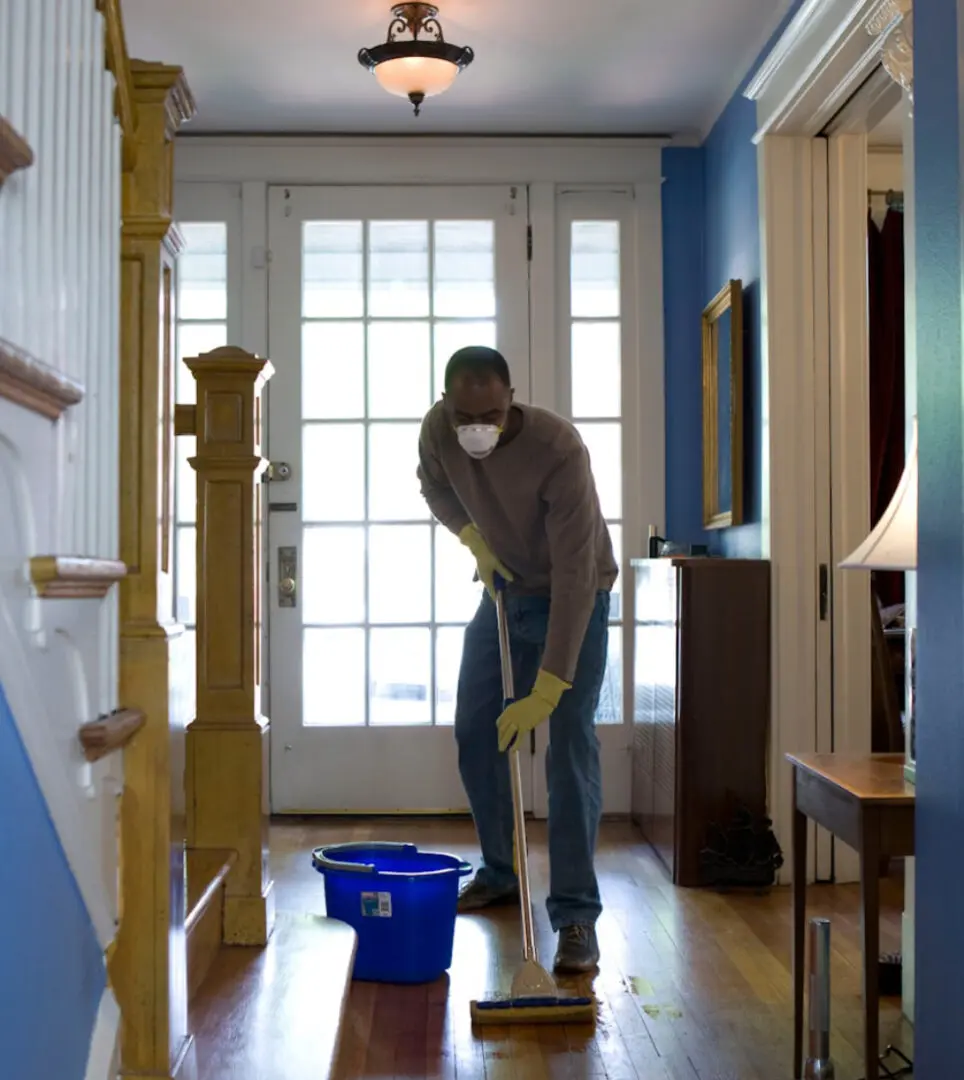Person mopping floor in a bright hallway with a blue bucket nearby.