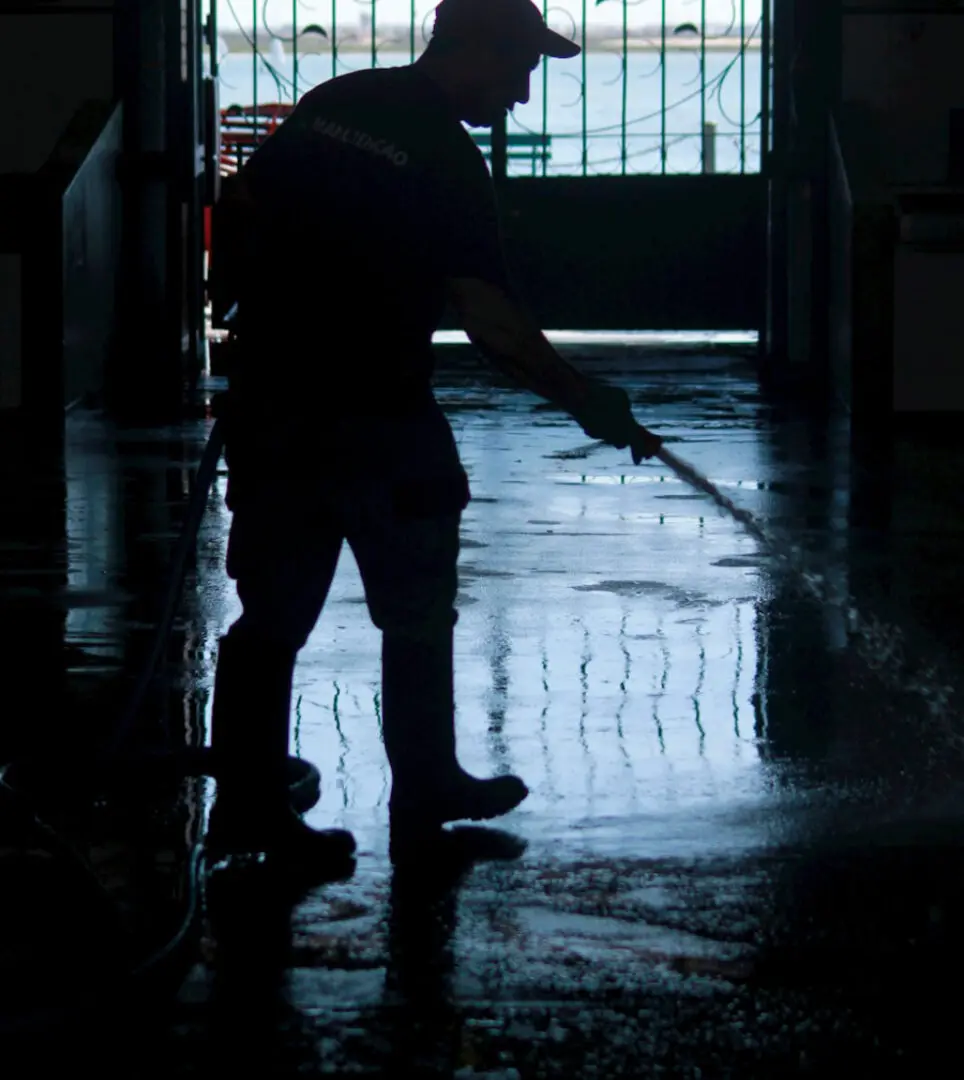 Silhouette of a person cleaning a wet floor indoors with a mop.