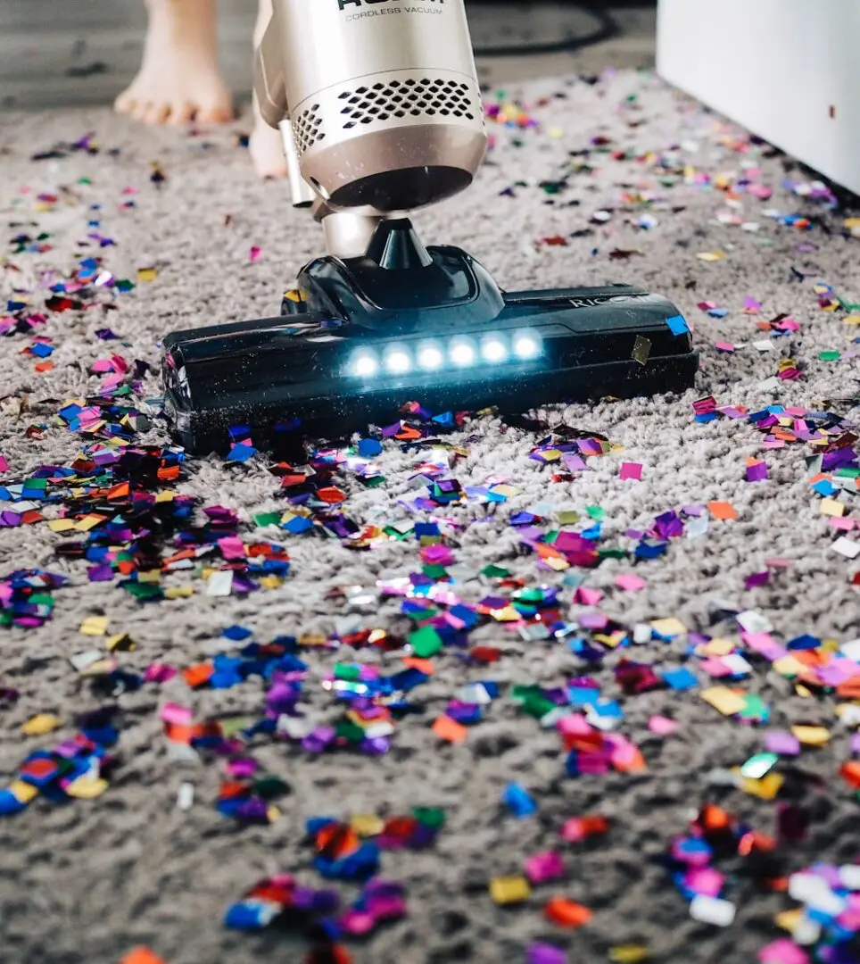 Vacuum cleaner picking up colorful confetti from carpet.