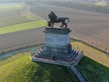 A large lion statue atop a stone pedestal on a grassy hill.