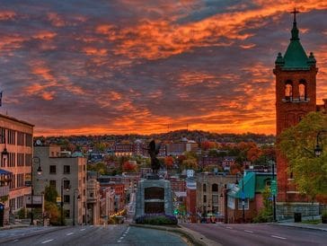 Sunset over a historic cityscape with vibrant clouds and a statue.