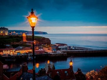 Coastal town at dusk with glowing street lamps and calm sea.