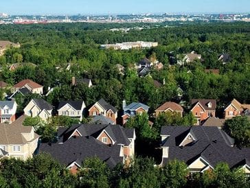 A suburban neighborhood surrounded by dense greenery under a clear sky.