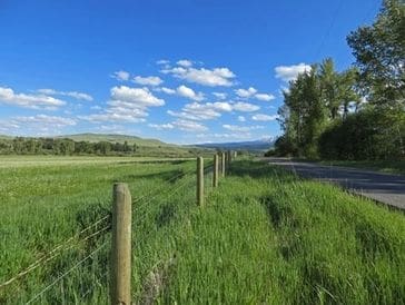 A peaceful rural landscape with a green field and a fence under a blue sky.