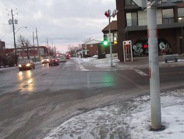 A snowy urban street intersection with cars and buildings.