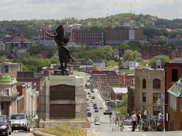 Statue of a person overlooking a city street and buildings.