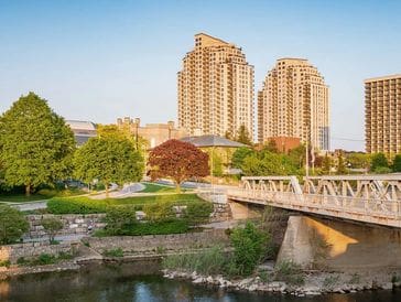 Two tall buildings overlooking a river and a small bridge on a sunny day.