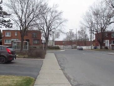 A quiet residential street with bare trees and brick houses on a cloudy day.