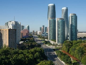 Modern cityscape with tall glass buildings and green trees under a clear sky.