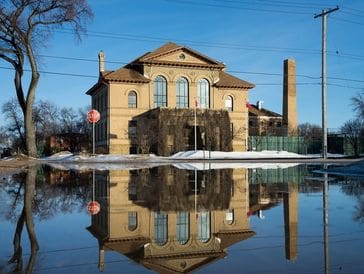 Historic building reflected in a large puddle on a sunny day.