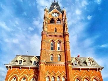 A tall red-brick clock tower against a blue sky with clouds.