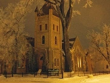 A tall, old brick building with a snowy foreground at night.