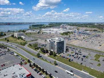 Aerial view of a commercial area with buildings, parking lots, and a river in the distance.