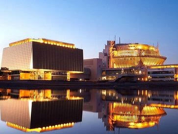 Modern buildings illuminated at dusk reflecting on calm water.