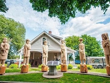 Traditional wooden statues in a serene garden with a house in the background.