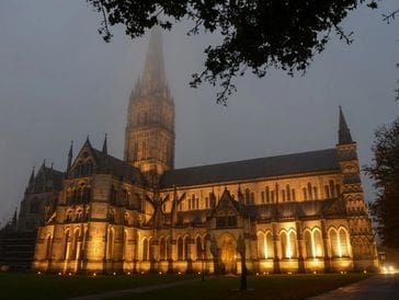 Illuminated gothic cathedral tower shrouded in fog at night.