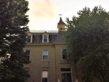 Historic brick building with a small steeple and cross at sunset.