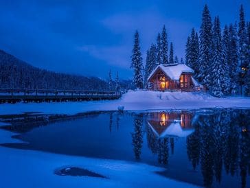 A cozy cabin by a snowy lake at twilight.