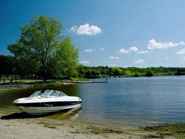Boat docked on a calm lakeshore with trees and blue sky.