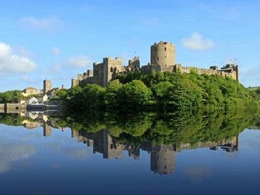 Historic castle reflected in calm river water on a clear day.
