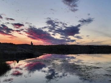 Sunset over a calm lake with colorful clouds reflecting on the water.