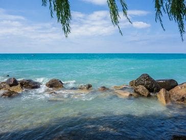 Tranquil ocean waves gently lap against rocky shore under a clear blue sky.