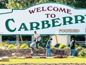 People working in front of a Welcome to Carberry sign.