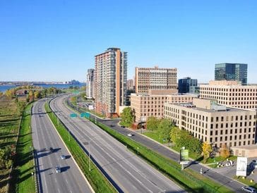 City highway with tall buildings and green spaces on a sunny day.
