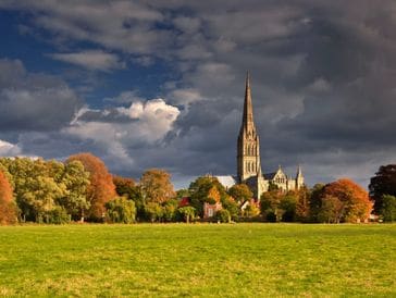 A tall church steeple rises above autumn trees under a cloudy sky.