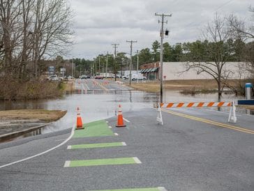 Road closed due to flooding with barriers and cones blocking access.