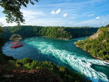 A vibrant river with swirling currents surrounded by lush greenery under a blue sky.