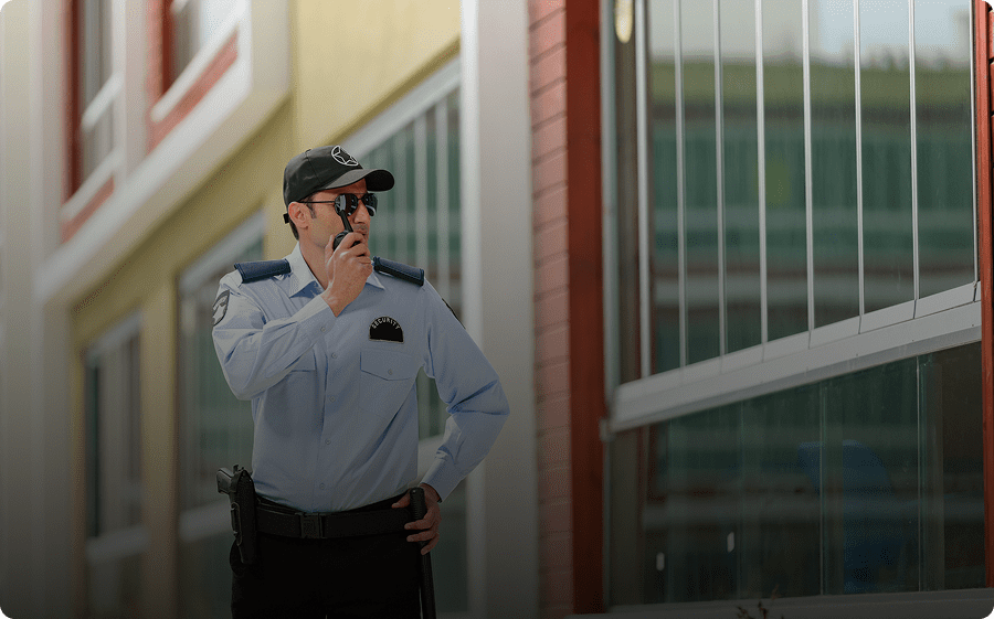A security guard stands alert, speaking into a walkie-talkie outside a building.