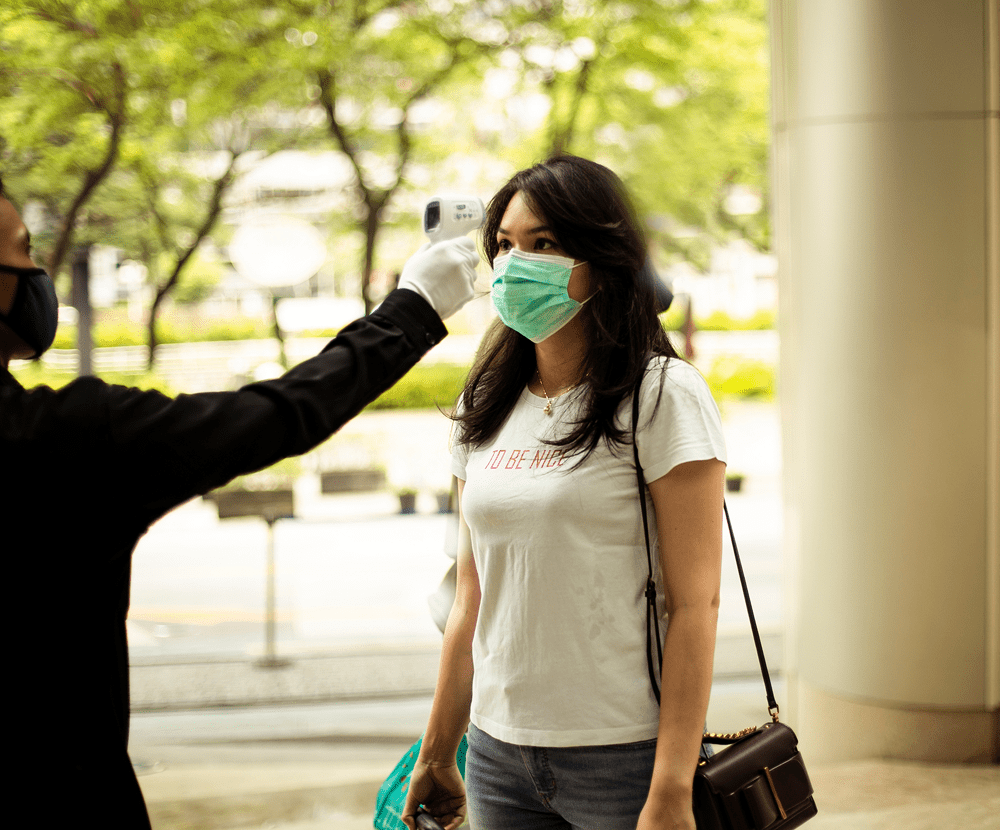 A woman wearing a mask having her temperature checked outdoors.