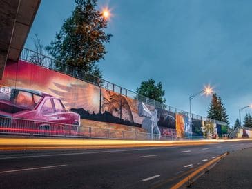 Colorful mural art on a city wall depicting urban scenes at dusk.