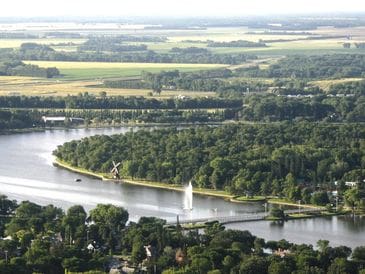A river curves through a green landscape with a sailboat and nearby houses.