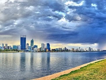 City skyline with dramatic clouds over calm river water.