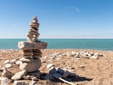 Stacked stones balanced on a rocky shore by the sea under a clear sky.