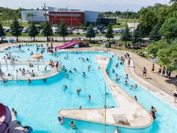 A lively public pool with people swimming and playing on a sunny day.