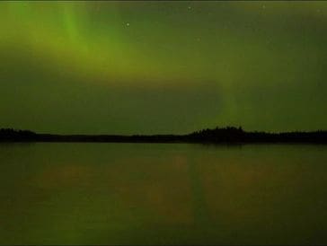 Northern lights glowing over a calm lake at night.