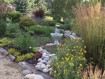 A lush garden with a stone-lined path and a white birdbath.