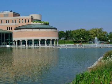 Modern building with a green roof beside a serene pond and fountain.